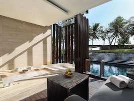 A modern outdoor pool area with a wooden deck, a seating area with a table, and a view of the pool.