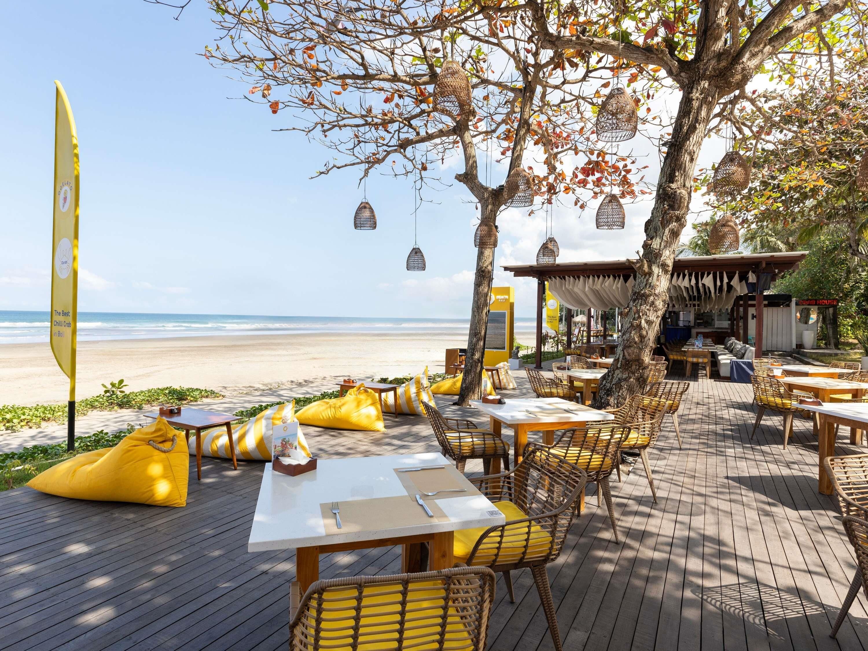Un espace de restauration en plein air avec des tables et des chaises, une vue sur la plage et des lanternes suspendues.