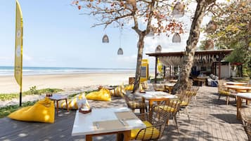 Un espace de restauration en plein air avec des tables et des chaises, une vue sur la plage et des lanternes suspendues.