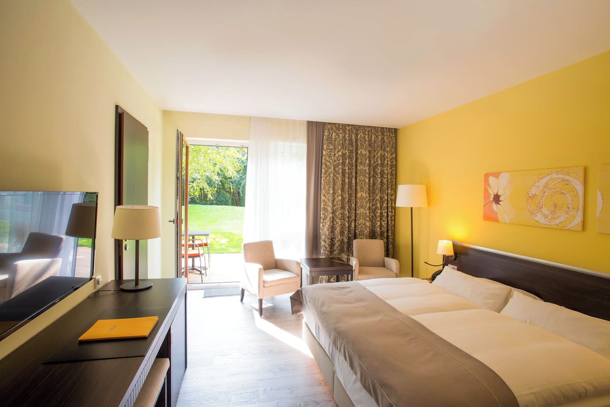 Habitación de hotel con cama, dos sillas, escritorio, televisor y vista al exterior.