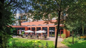 A courtyard with outdoor seating, a garden, and a building with large windows and a red door. - Heide Spa Hotel & Resort (Bad Dueben)