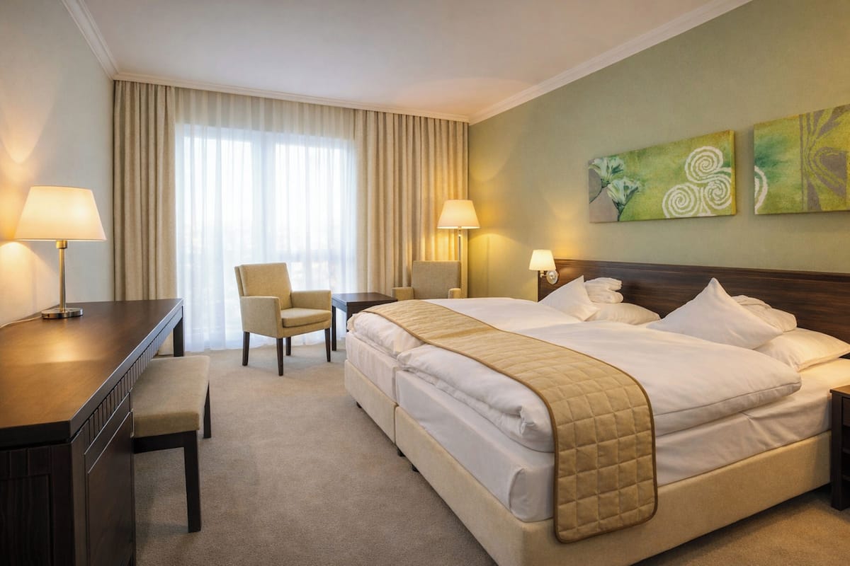 Una habitación de hotel con una cama grande, dos mesitas de noche, un escritorio, una silla y una ventana con cortinas.