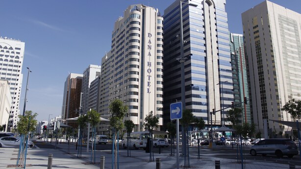 A modern hotel with a prominent 'HOTEL' sign, surrounded by tall buildings and a clear blue sky.
