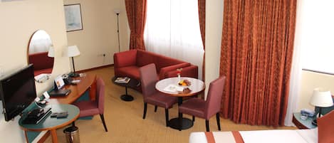 A hotel room with a bed, a desk with a computer, a chair, a small table with fruit, and a TV.
