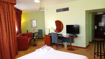 A hotel room with a bed, a desk with a computer, a TV, a chair, a small table with a lamp, and a sofa.