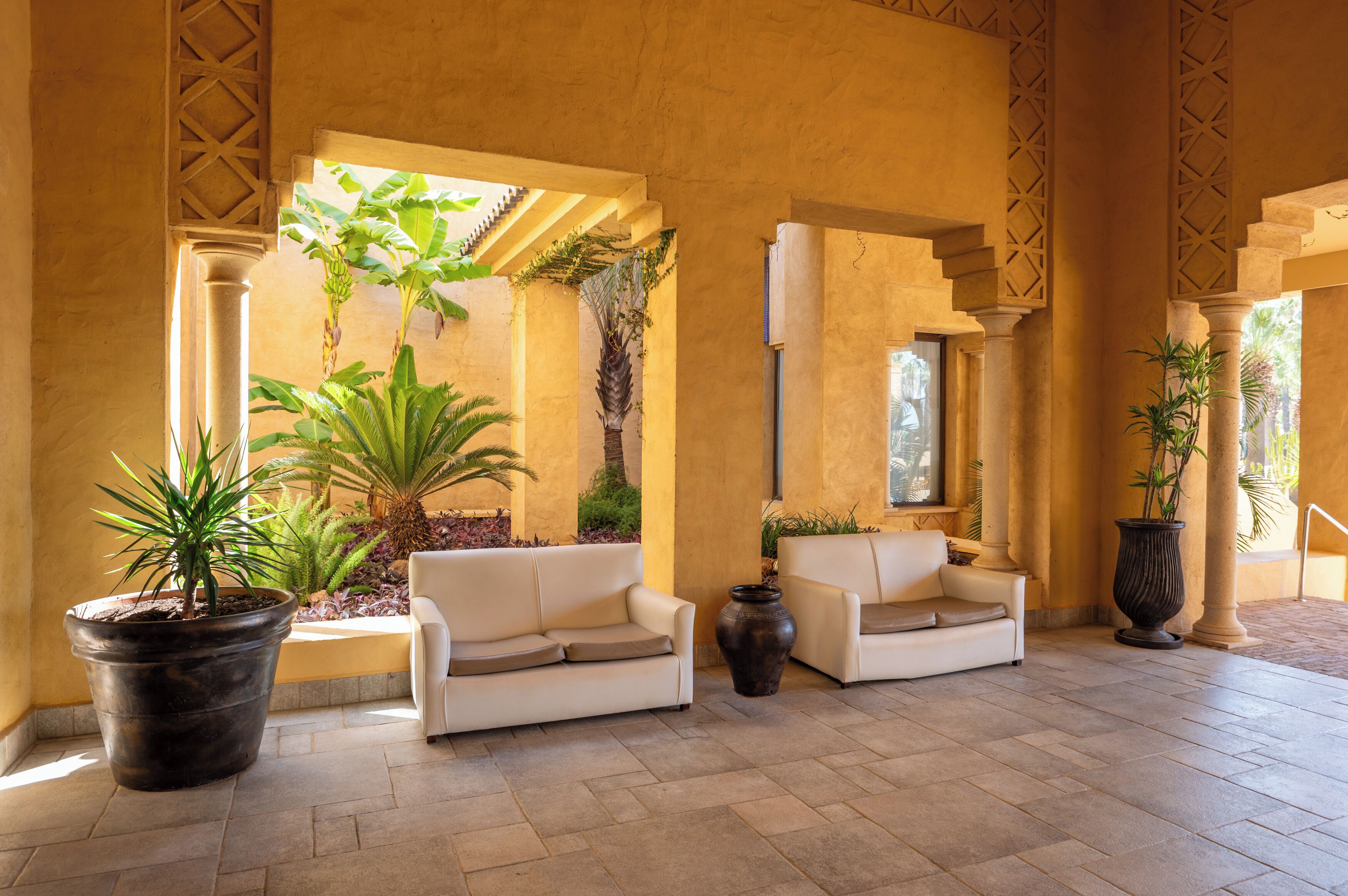 A spacious lobby with two sofas, large potted plants, and a tiled floor.