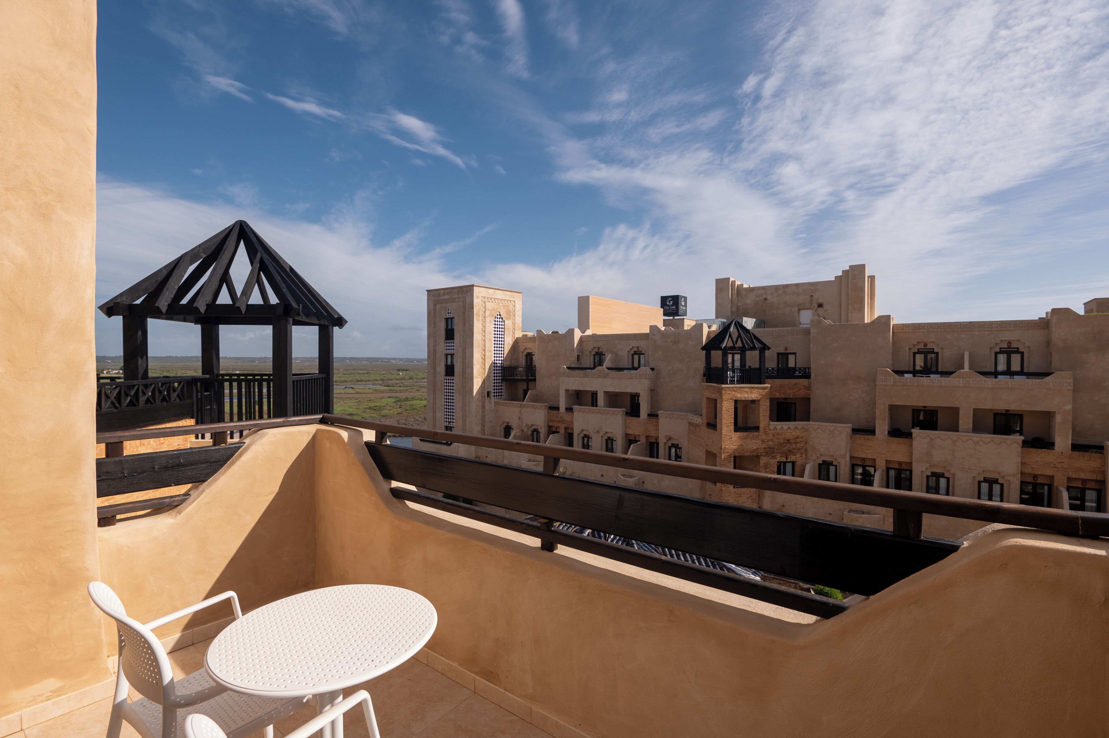 A balcony with a table and chairs, a wooden gazebo, and a view of traditional buildings.