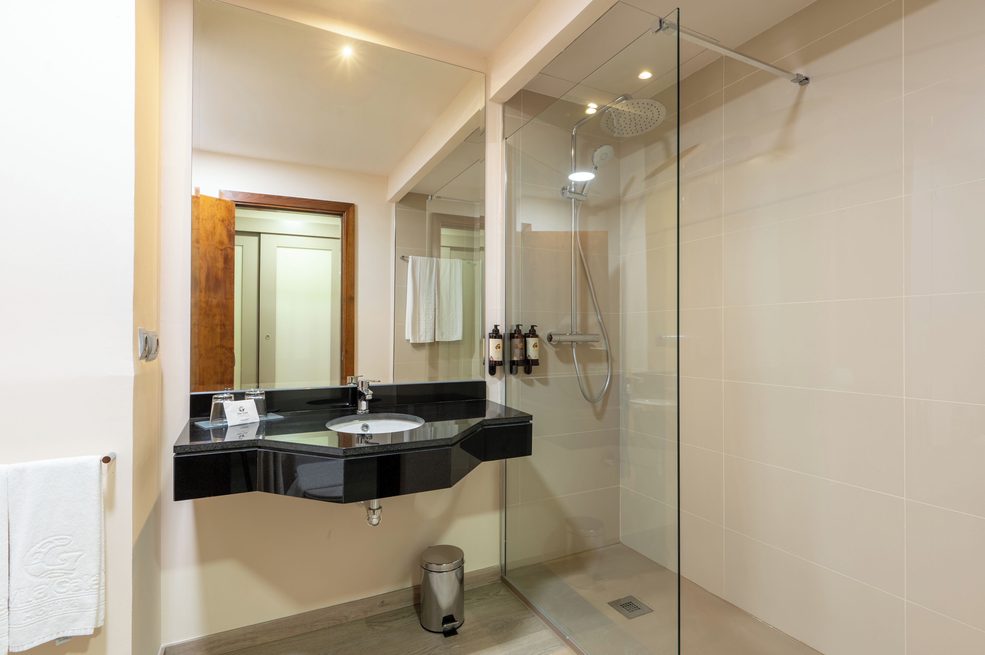Un baño moderno con ducha acristalada, tocador con lavamanos negro y espejo.