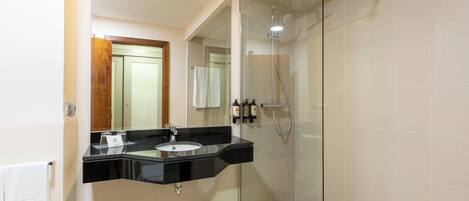 Un baño moderno con ducha acristalada, tocador con lavamanos negro y espejo.