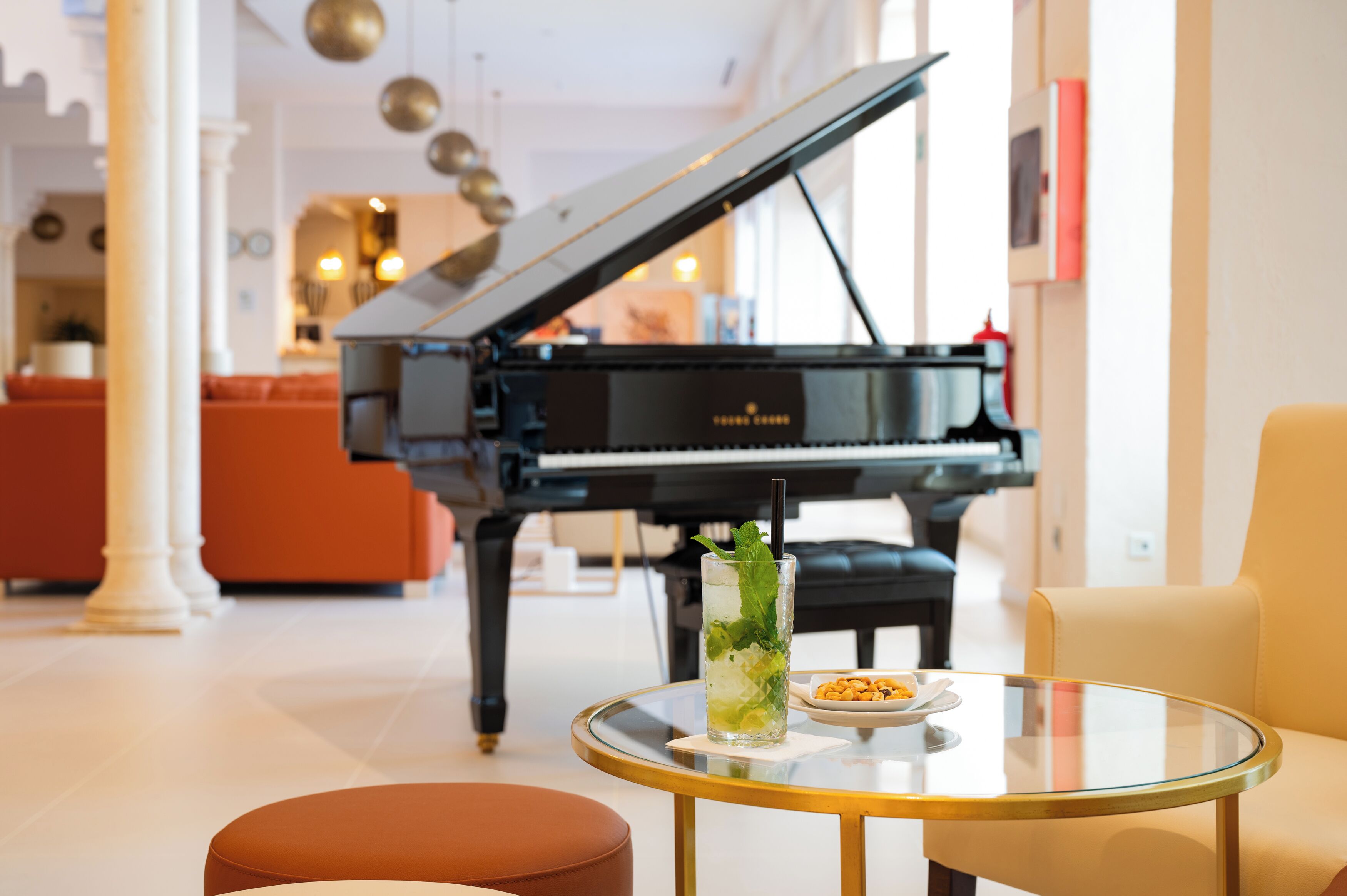 A grand piano in a well-lit room with a glass table and a chair.
