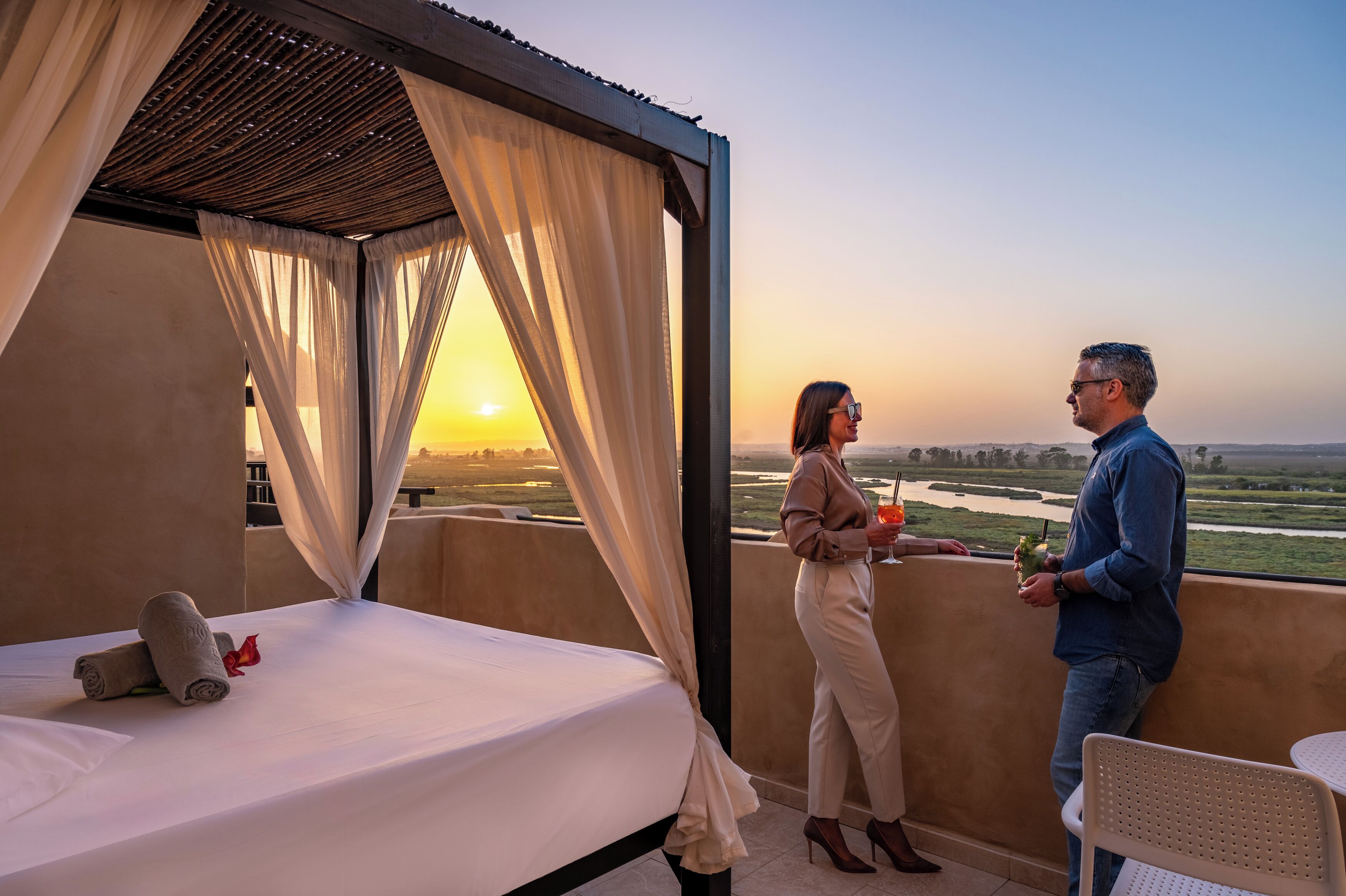 A balcony with a bed, a table, and a view of a landscape.
