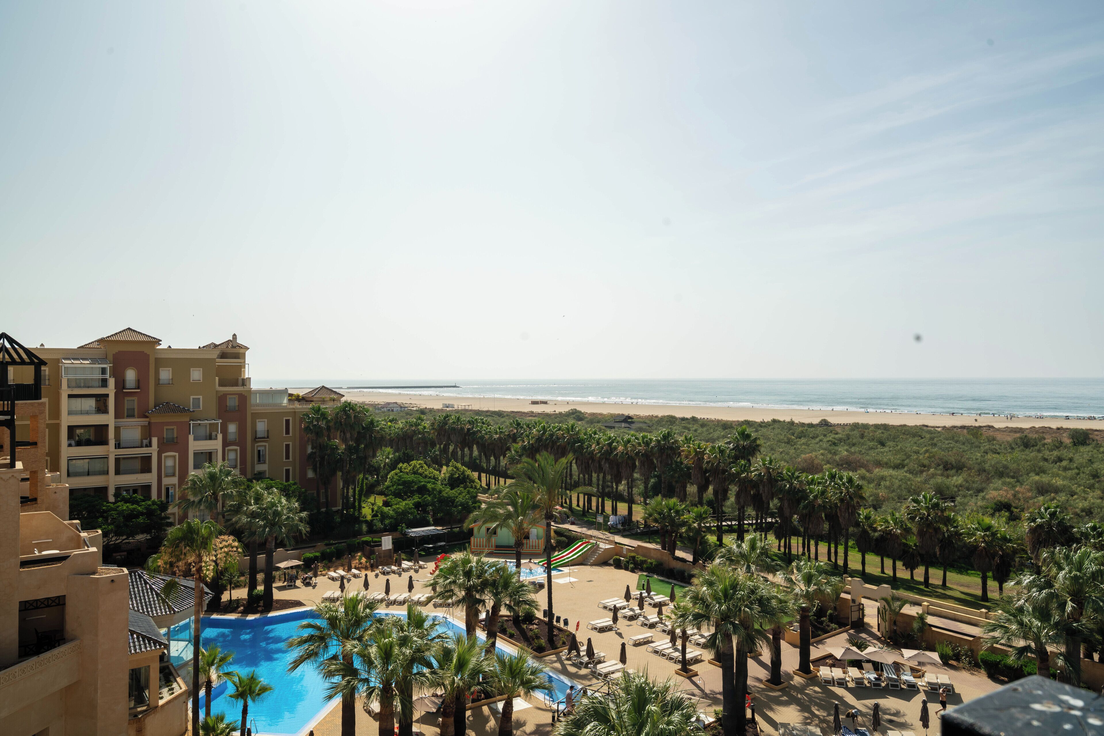 A resort with a swimming pool, beach view, and palm trees.