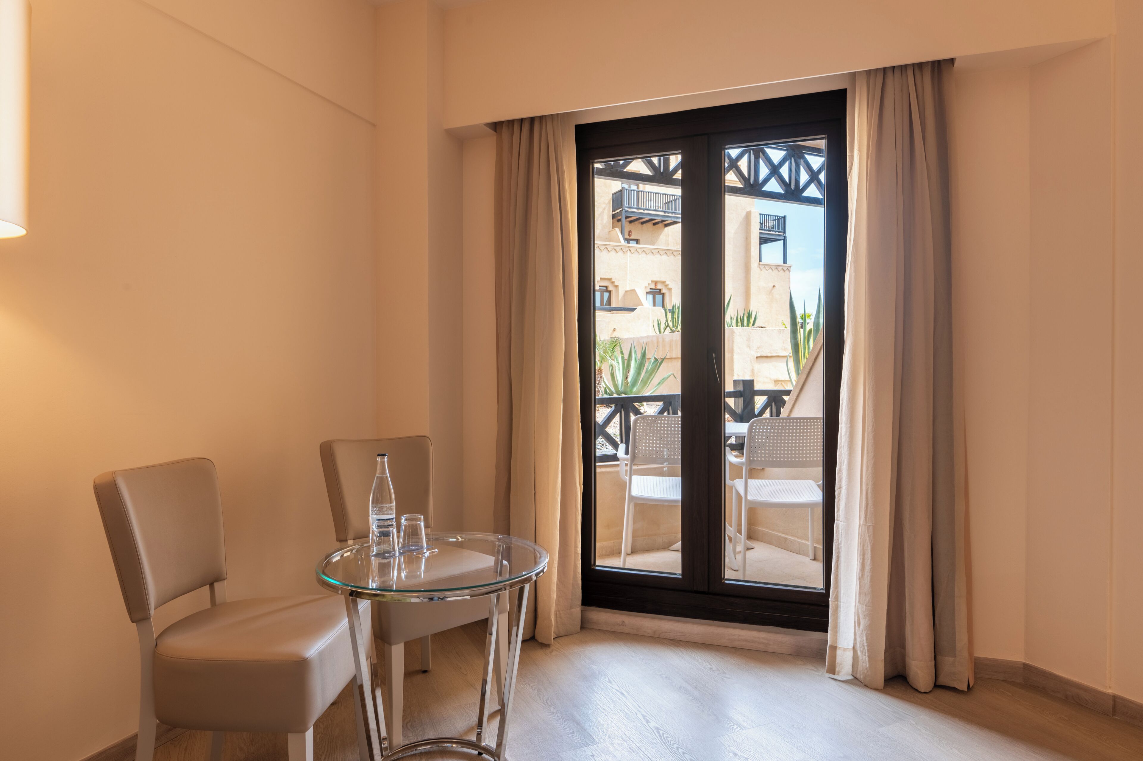 Une pièce avec une table en verre, deux chaises et une porte-fenêtre coulissante donnant sur un espace extérieur avec un balcon.