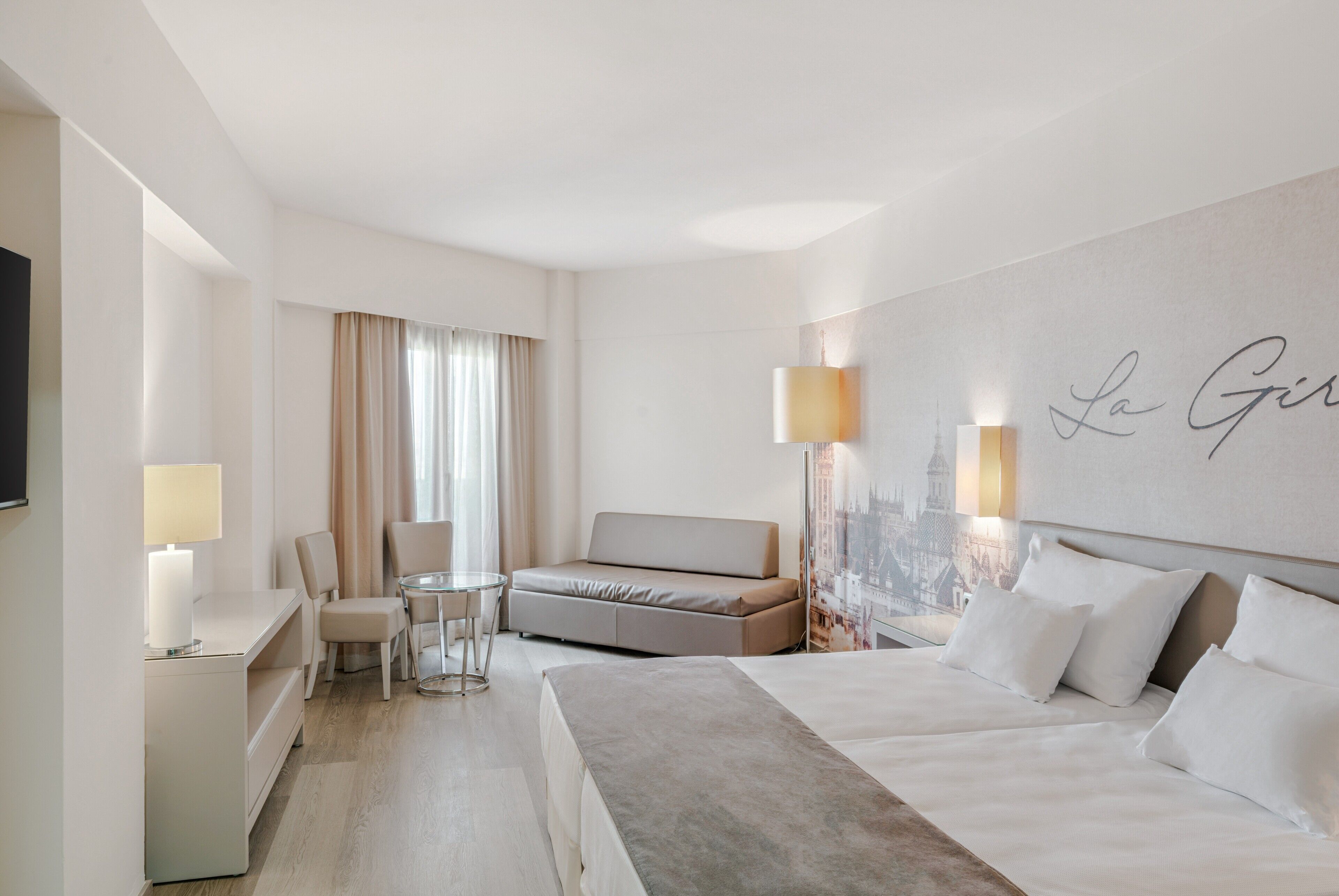 A hotel room with a bed, a sofa, a desk, a chair, and a lamp.