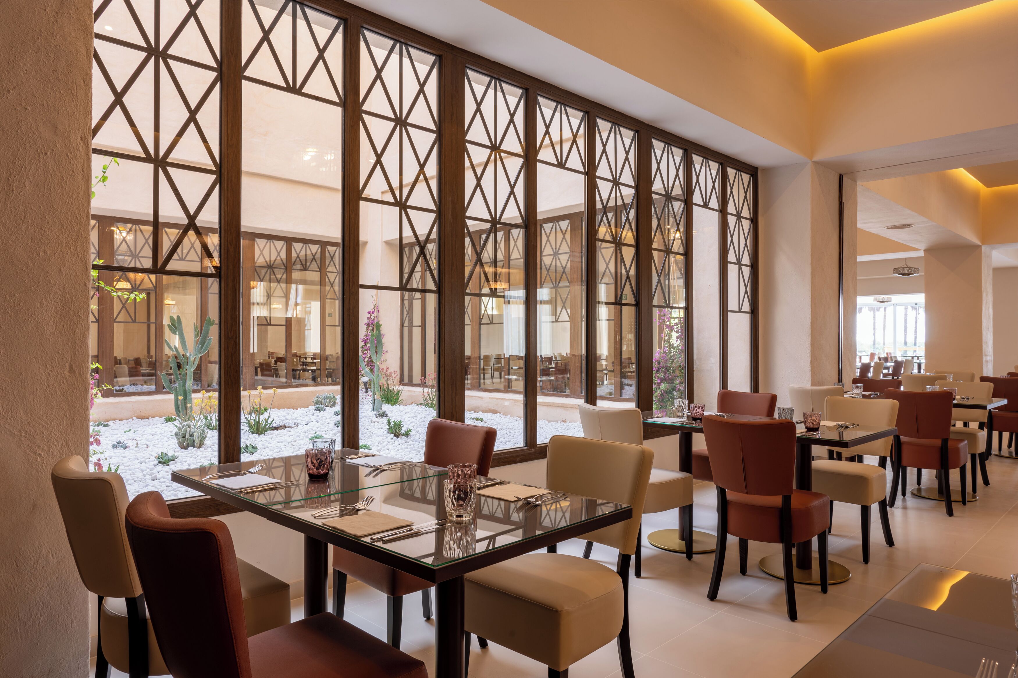 Un comedor con mesas y sillas, ventanas amplias con vista a un patio interior, y una decoración moderna.