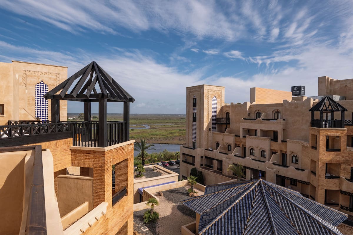 Ein Hotel mit Terrasse, Blick auf ein Gewässer und traditioneller Architektur.