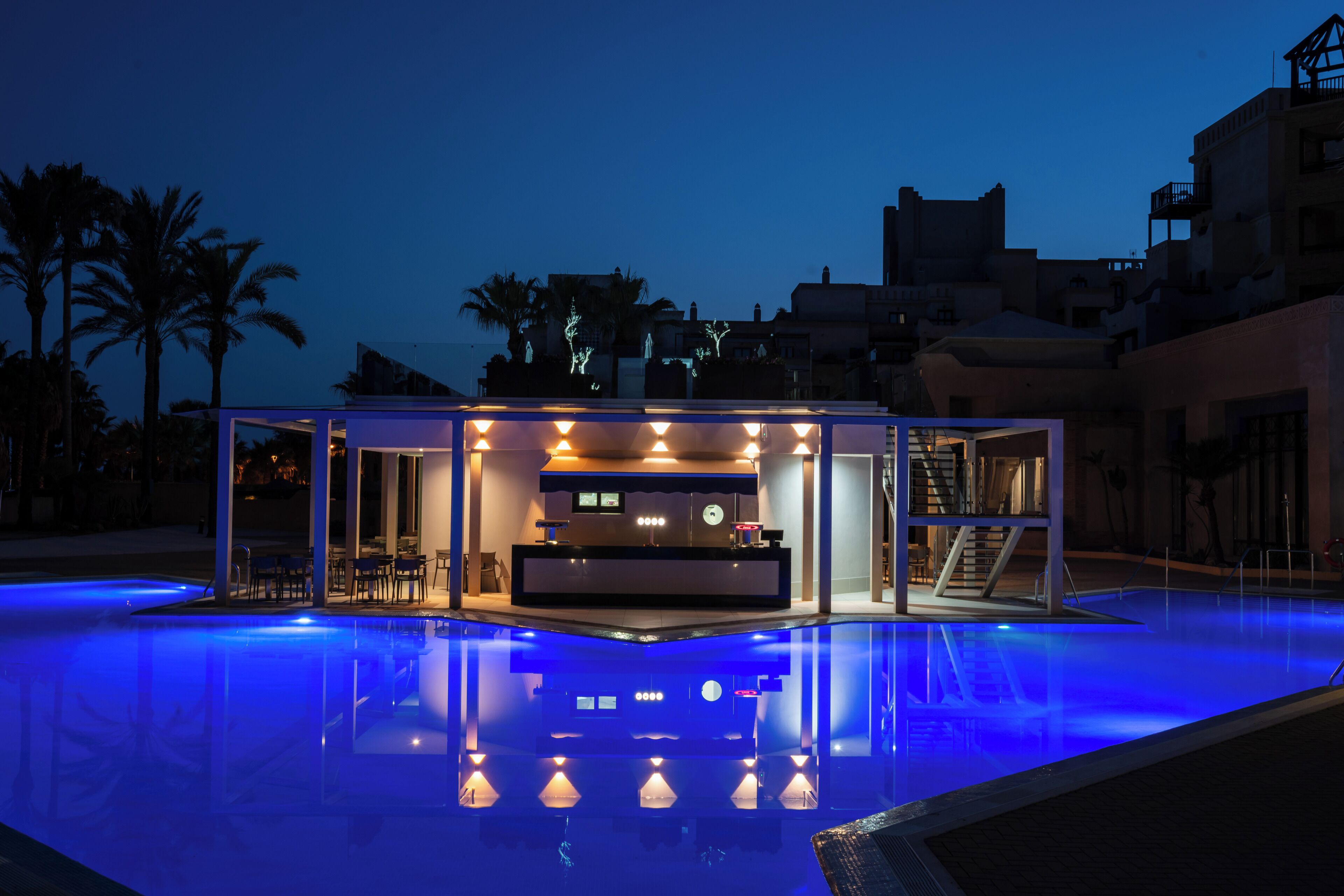 Un bar junto a la piscina con mostrador, zona de estar y una escalera que lleva a un nivel superior.