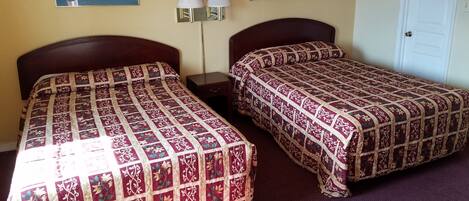 Habitación de hotel con dos camas, cada una con una colcha estampada, una mesita de noche con lámpara y dos cuadros enmarcados en la pared.