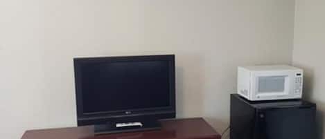 A room with a wooden dresser, a television, and a microwave.