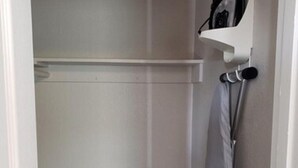 Pequeño cuarto cerrado con suelo de madera, pared blanca y estante blanco con un bolso colgado.