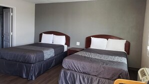 Habitación de hotel con dos camas, cabeceros de madera y una mesita de noche pequeña.