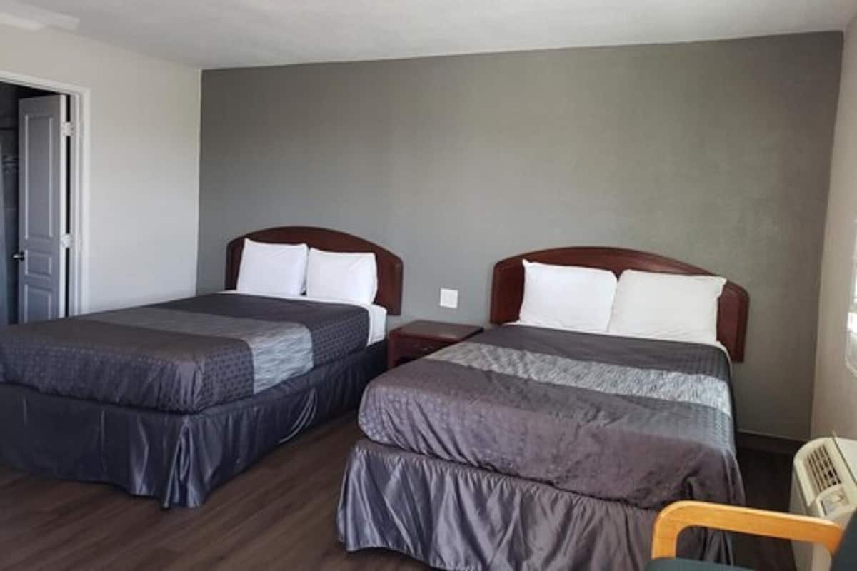 A hotel room with two beds, wooden headboards, and a small bedside table.