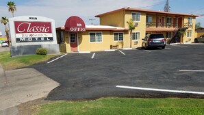 Un motel Classic Inn & Suites con un toldo rojo, un estacionamiento y un edificio de dos pisos con fachada amarilla.