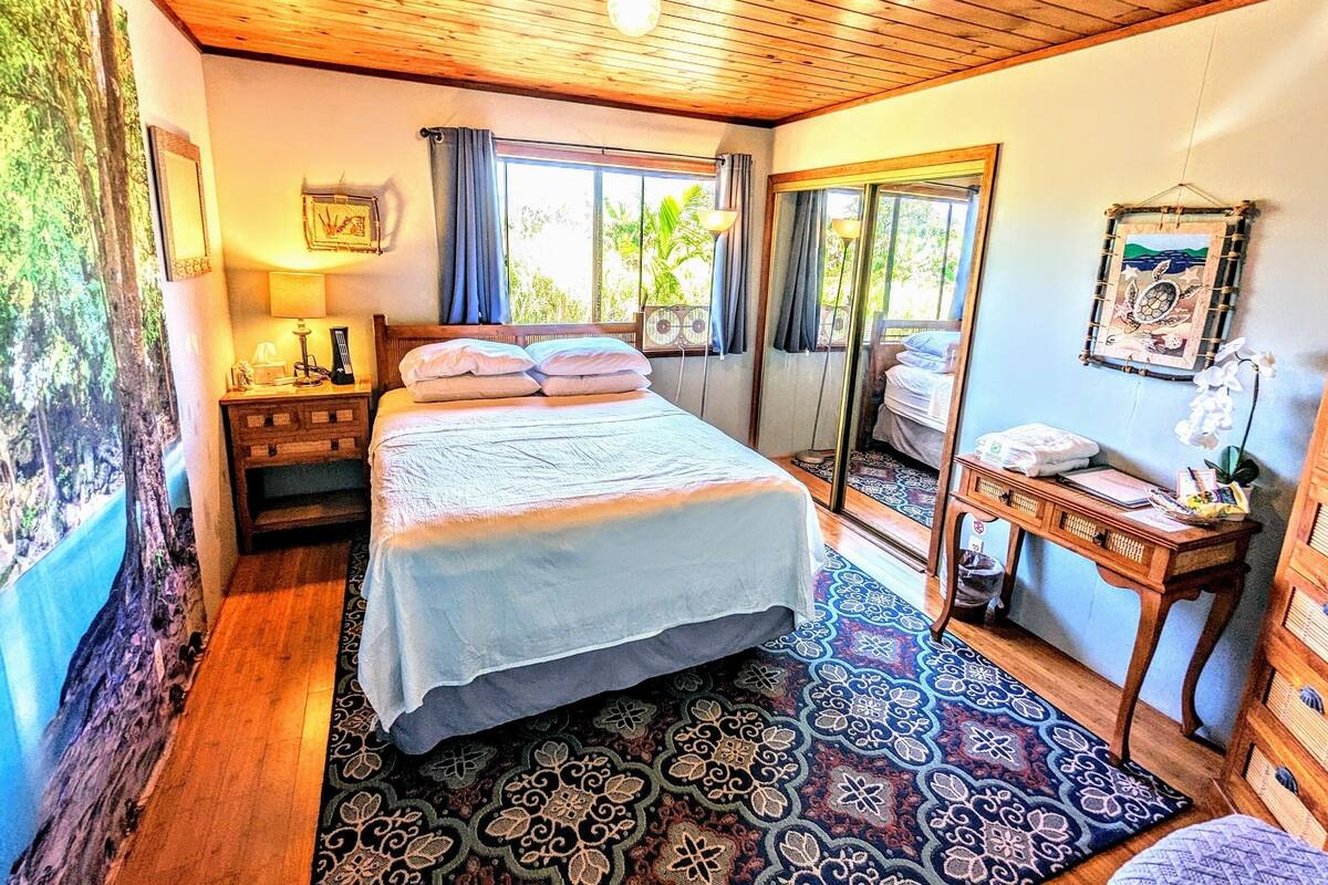 Ein Schlafzimmer mit Bett, Nachttisch, Spiegel und Blick ins Freie.