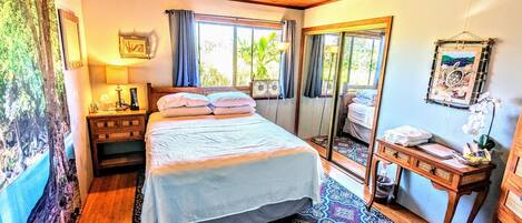 Un dormitorio con cama, mesita de noche, espejo y vistas al exterior.