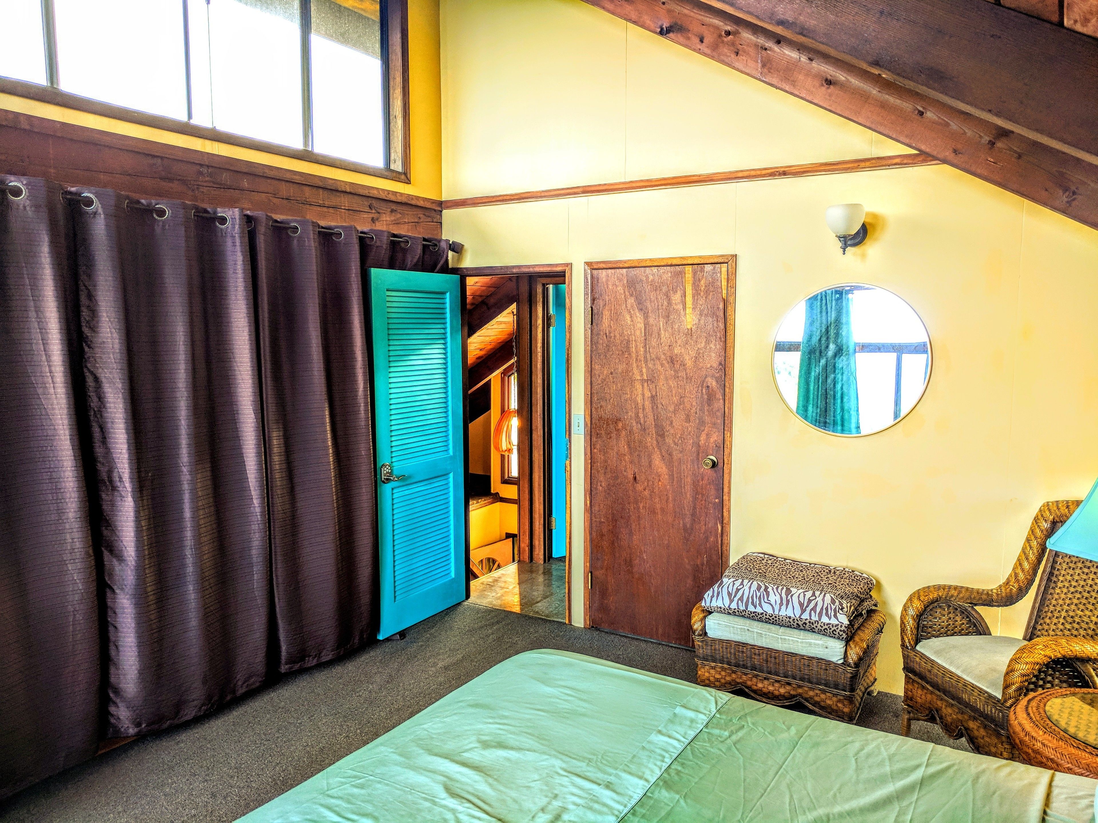 A room with a bed, a chair, a wooden door, and a window with curtains.