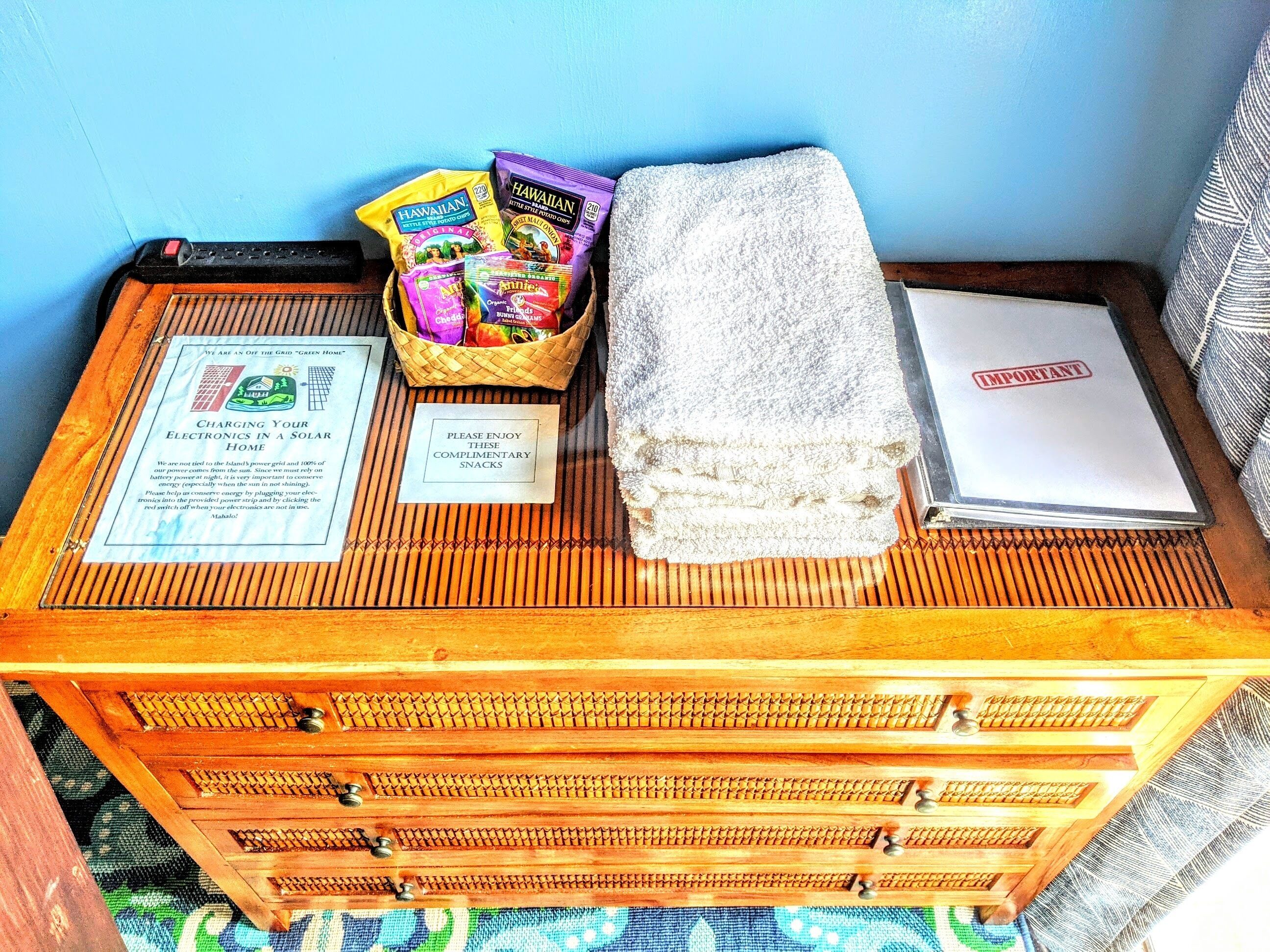 A wooden chest with a sign about solar charging, a basket of snacks, a towel, and a white folder with a red stamp.