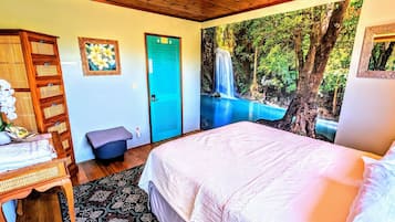 Un dormitorio con cama, escritorio, silla, taburete pequeño, puerta azul y un mural de cascada en la pared.