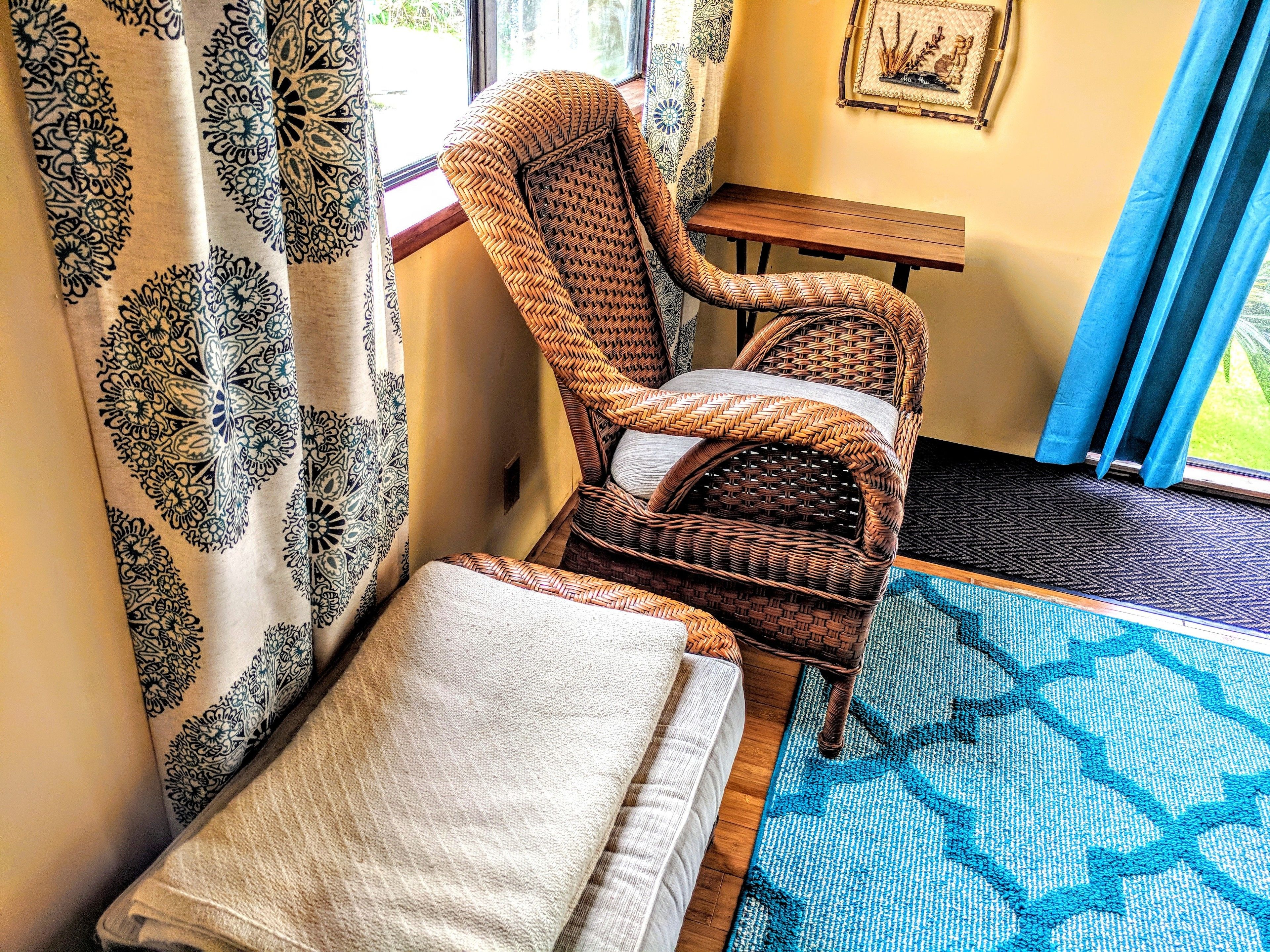 A wicker chair with a cushion, a small wooden table, and a patterned rug.