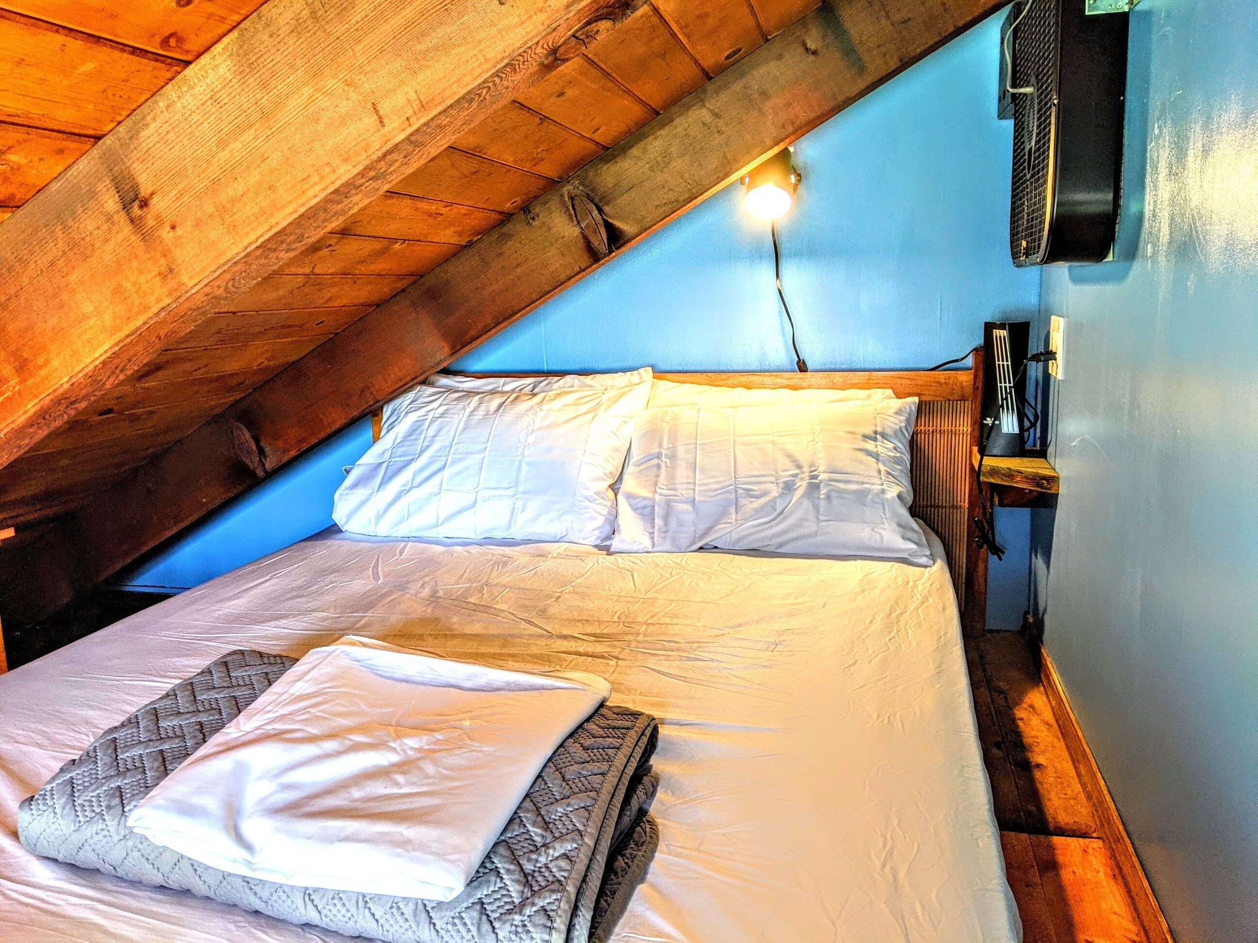 Un dormitorio con techo inclinado, una cama con ropa de cama blanca, una mesita de noche y un calentador fijado a la pared.