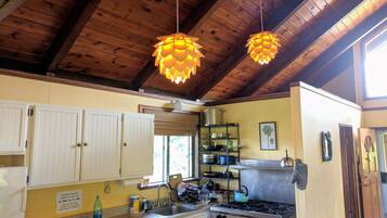 Una cocina con vigas de madera, armarios blancos, estufa y luces colgantes.