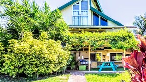 Une maison à deux étages, dotée d’un toit à pignon, d’un porche couvert et d’un petit espace extérieur aménagé pour s’asseoir.