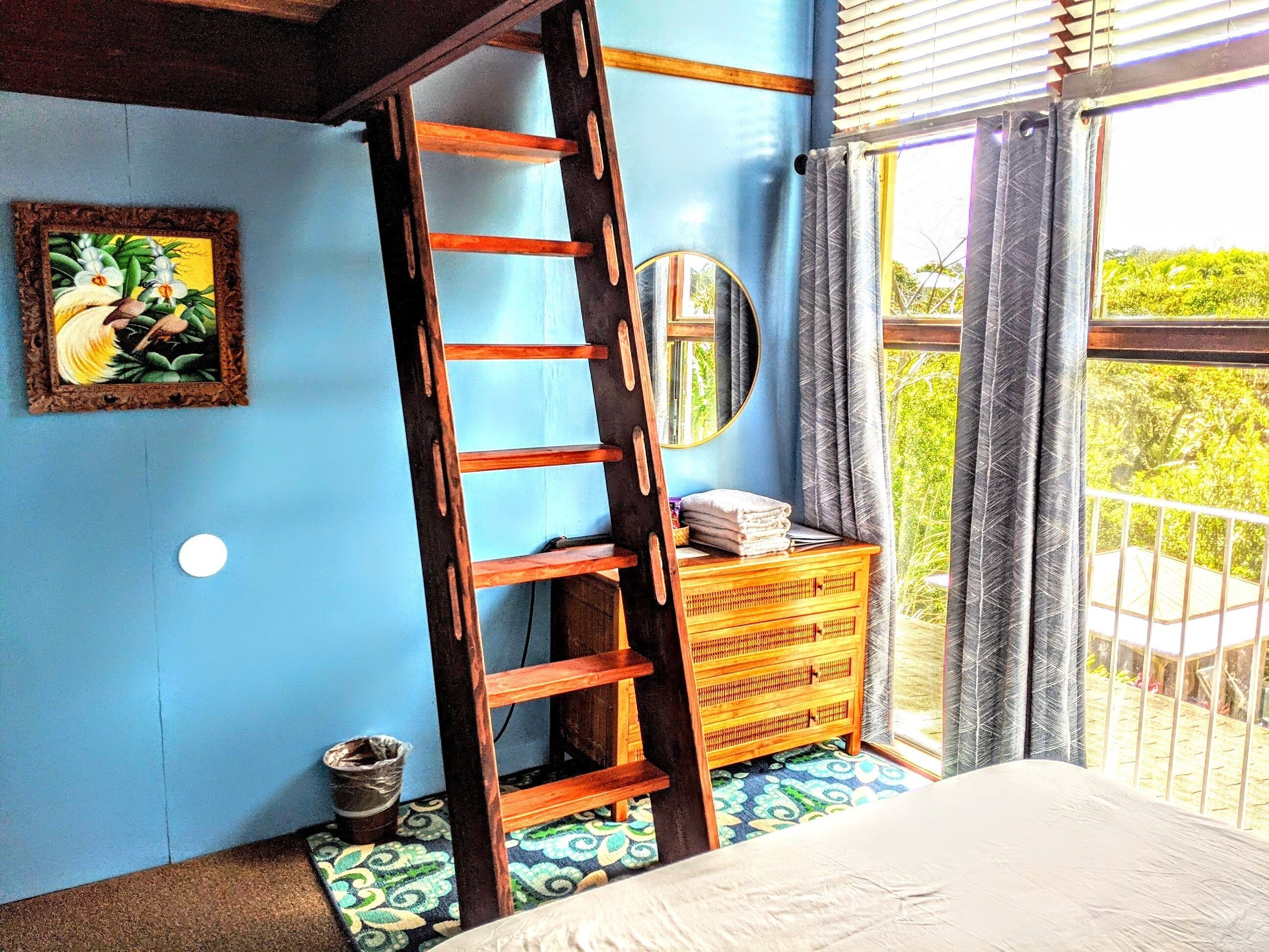 A bedroom with a wooden ladder, a dresser, a mirror, and a window with curtains.