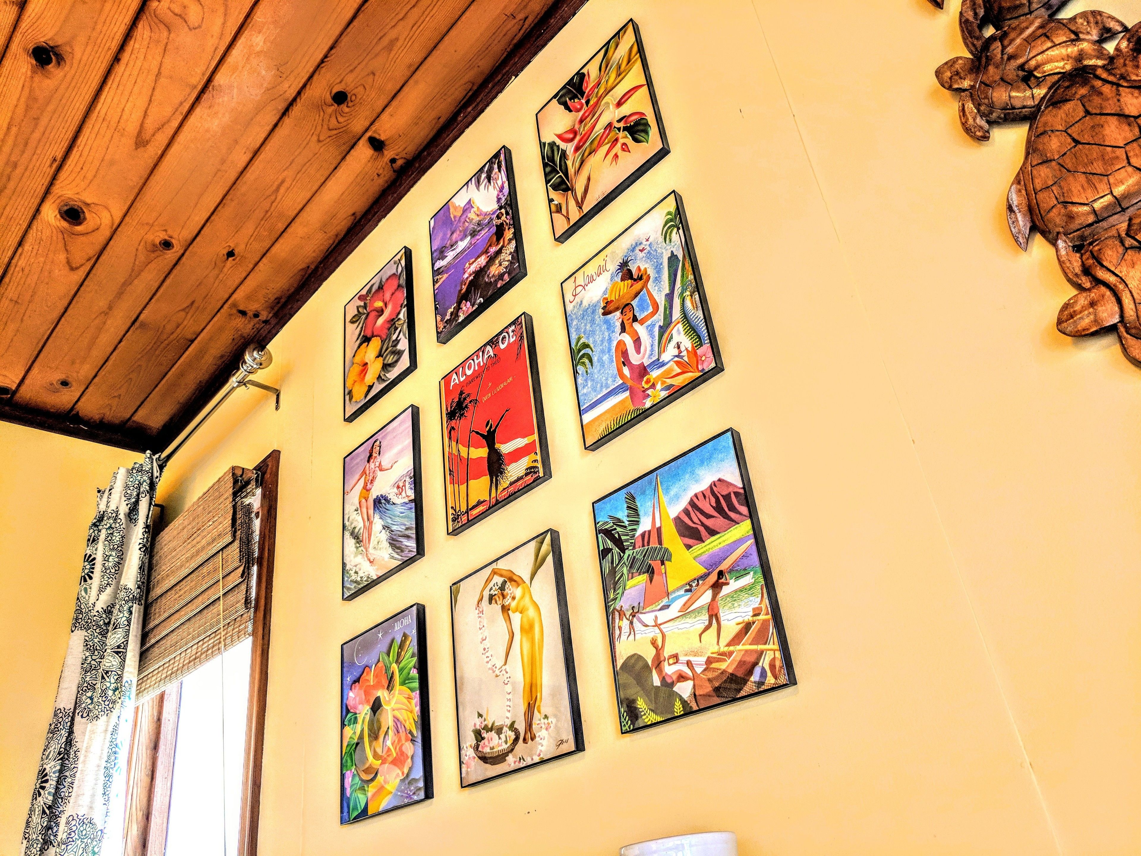 Una pared con varios cuadros enmarcados que muestran escenas tropicales y figuras.