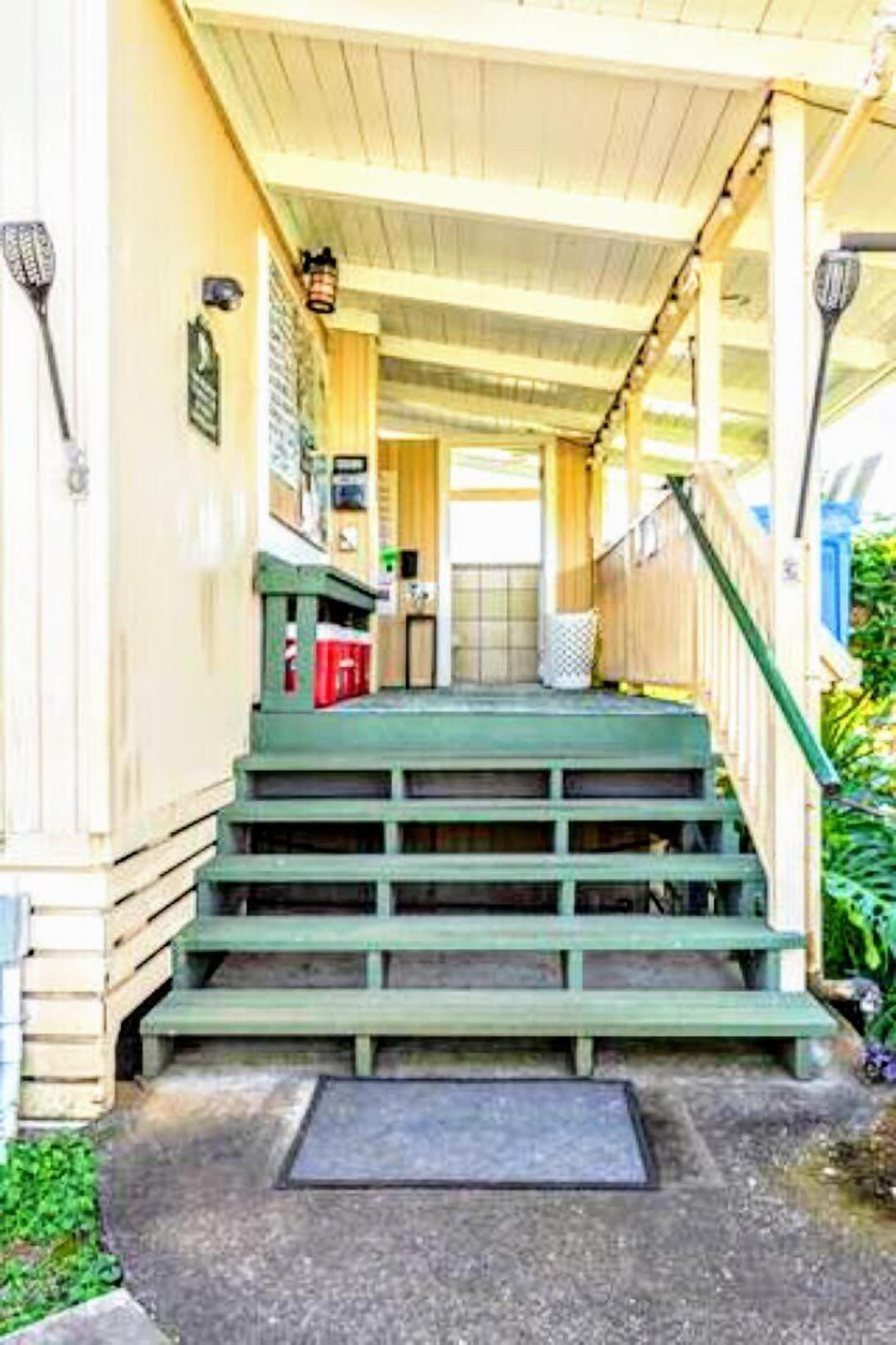 A covered porch with green steps leading to a door.