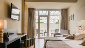 Habitación de hotel con escritorio, dos camas, televisión y vistas al patio exterior.