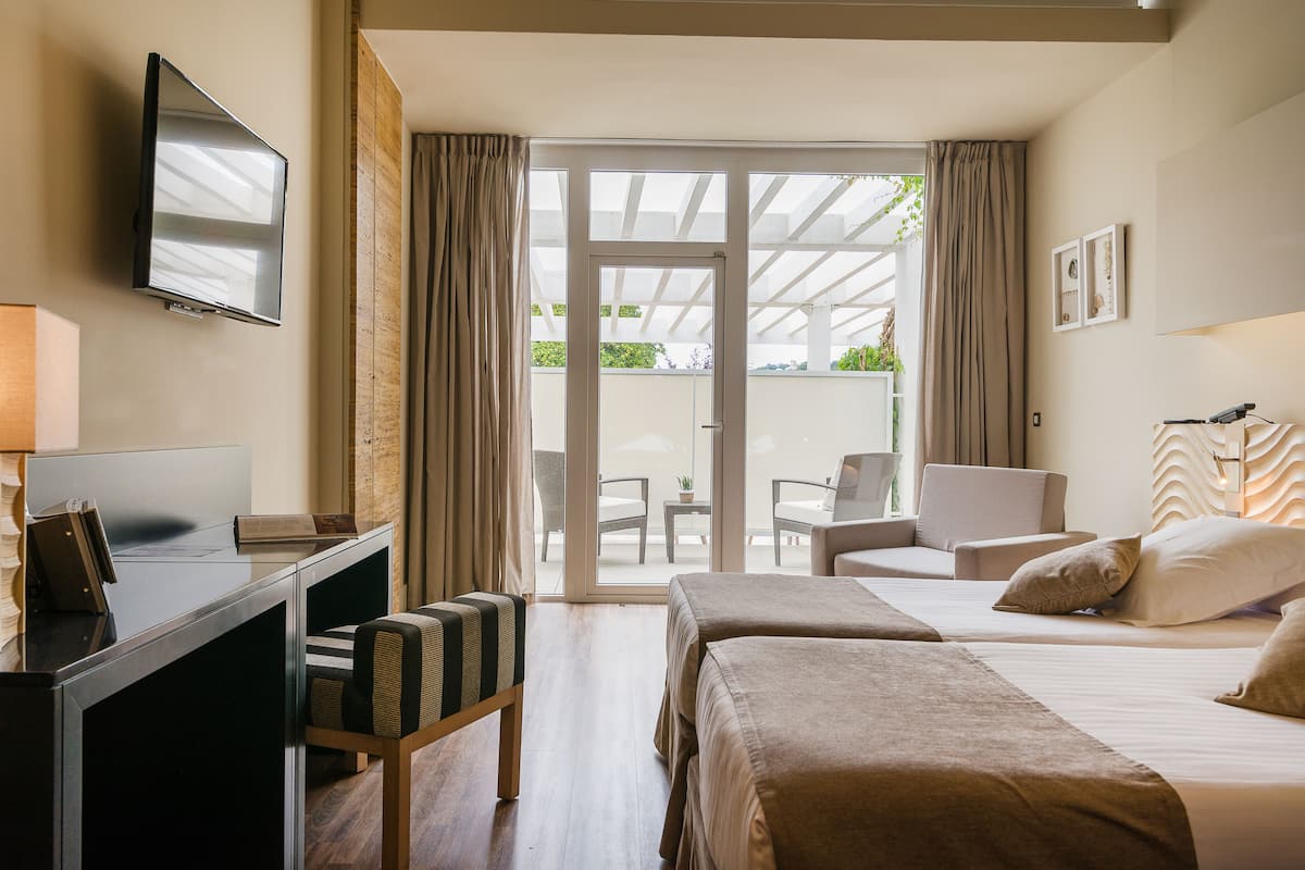 A hotel room with a desk, two beds, a TV, and a view of the outdoor patio.