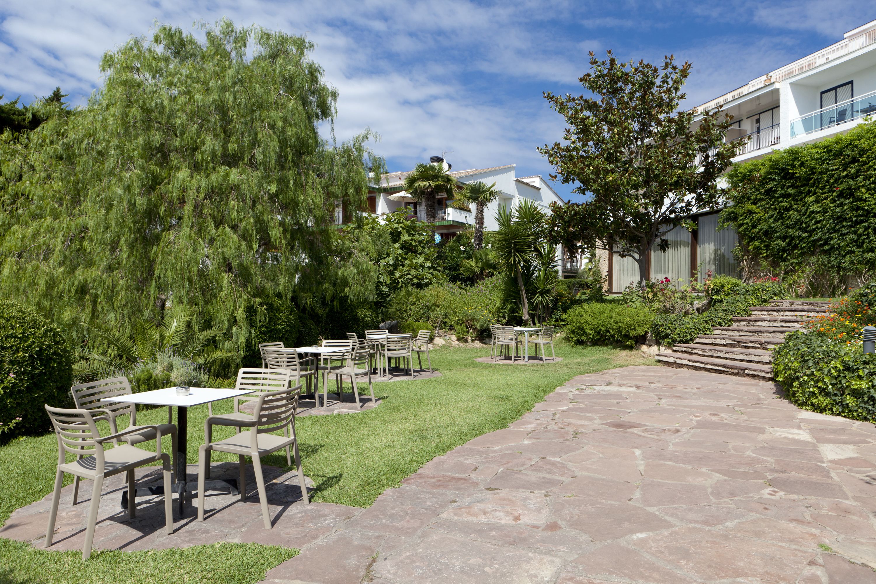 A patio area with stone flooring, outdoor furniture, and lush greenery.