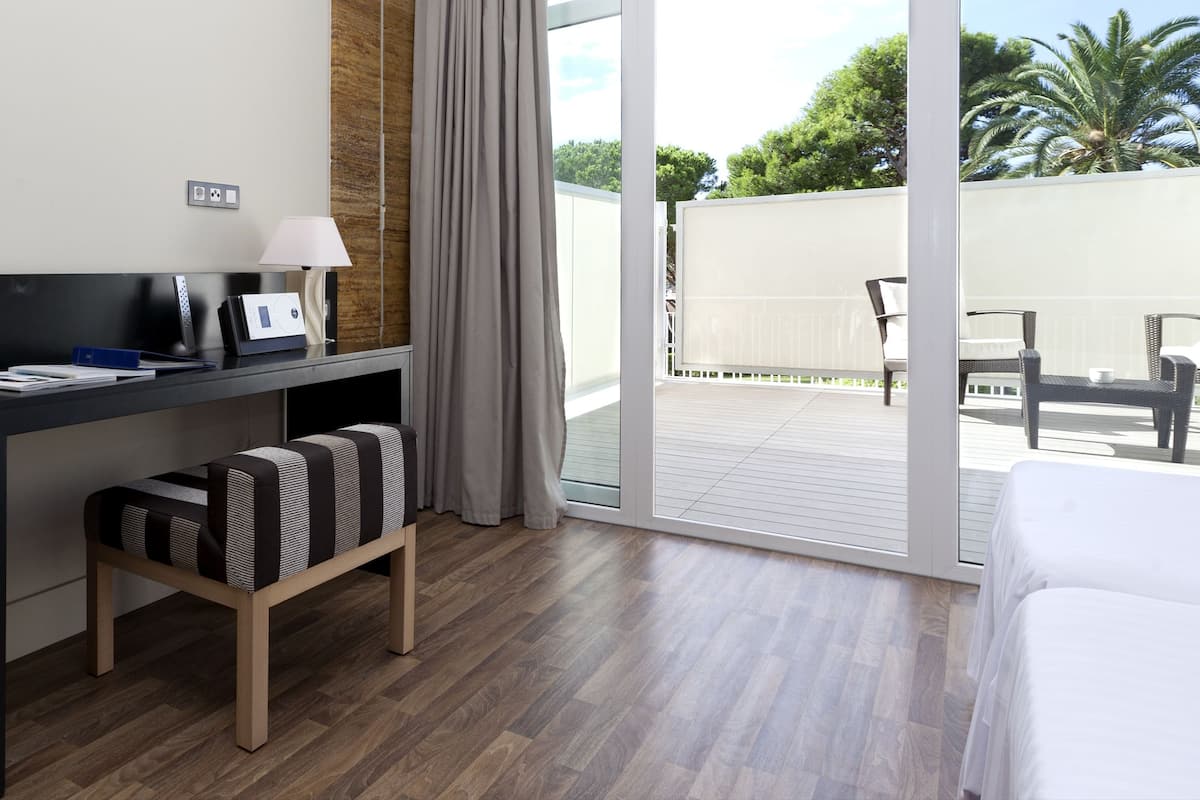 A hotel room with a bed, a desk with a lamp, a chair, and a view of the outdoor patio.