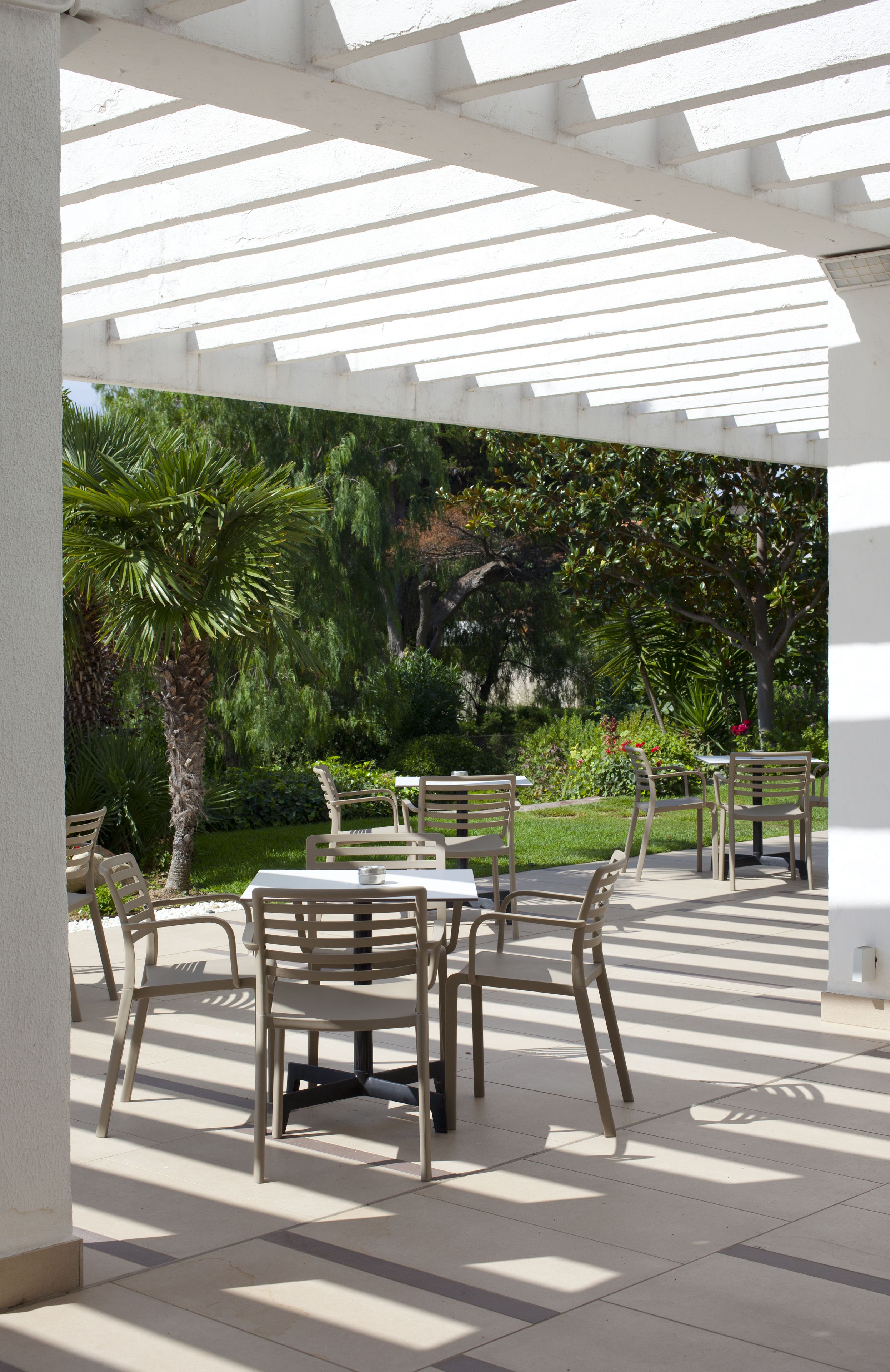 Un espacio de patio al aire libre con pérgola blanca, mesas y sillas.