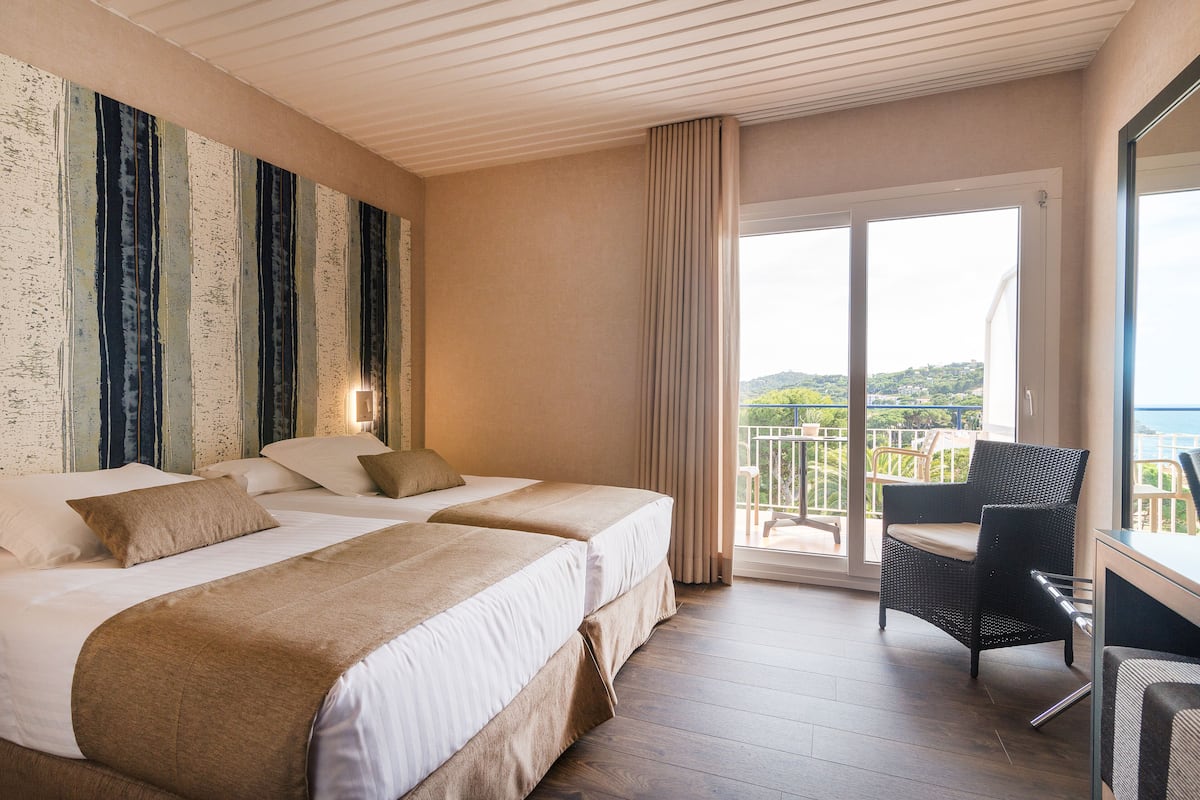 Une chambre d’hôtel avec deux lits, un balcon avec une chaise et une vue sur le paysage.