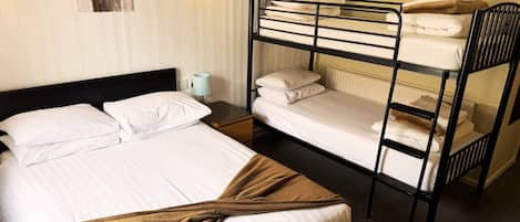 Habitación con literas, una cama individual, una mesita de noche, una lámpara y una luz empotrada en la pared.