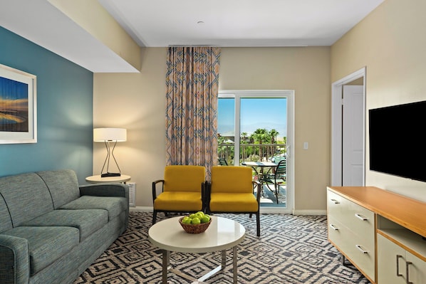 A hotel room with a sofa, two yellow chairs, a table with a fruit bowl, a TV, and a patterned carpet. - WorldMark Indio (Indio)