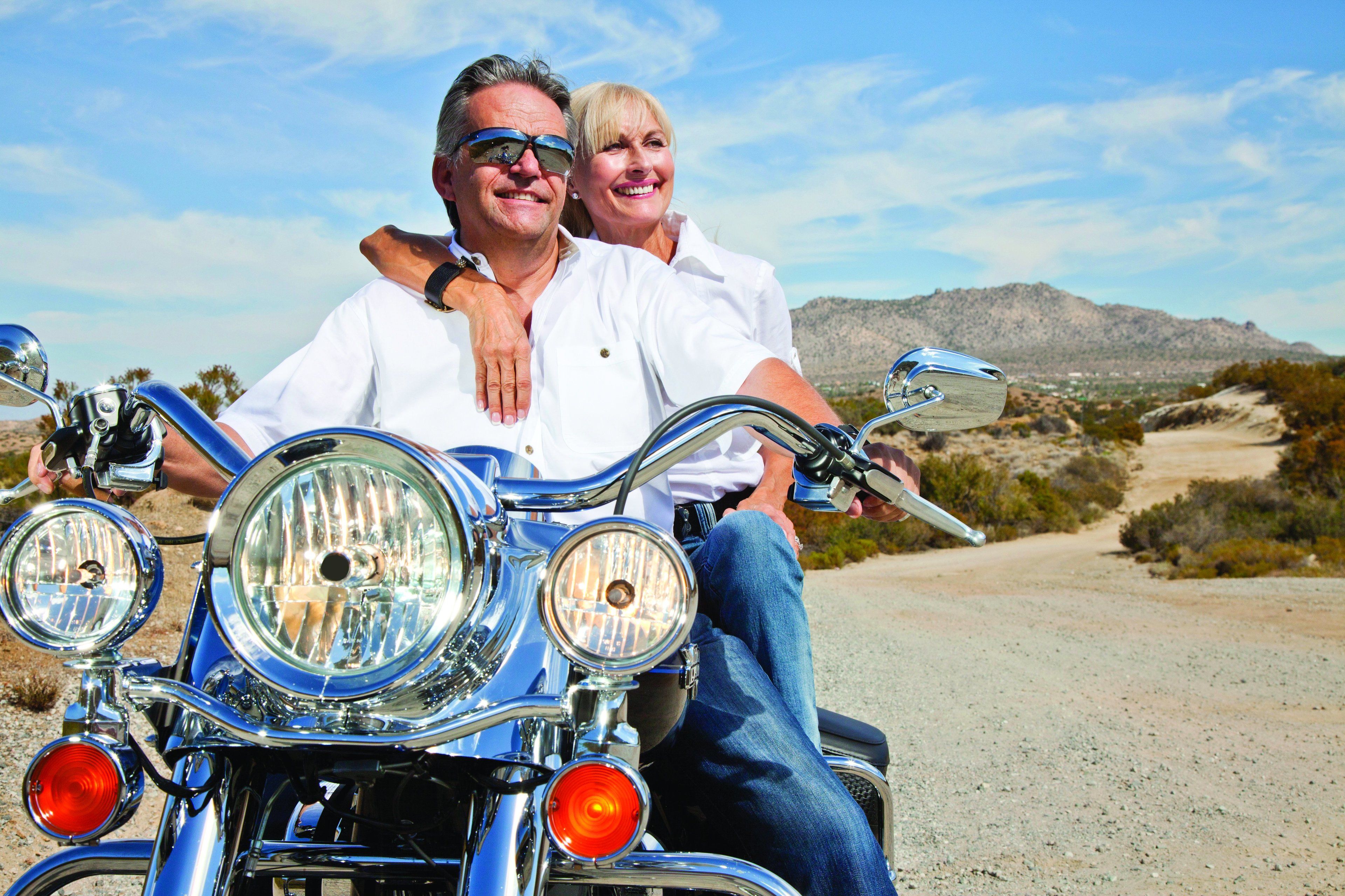 A motorcycle with two riders, a desert landscape, and mountains in the background.