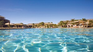 En pool med kristallklart vatten, omgiven av solstolar och parasoller, och inramad av hotellbyggnader.
