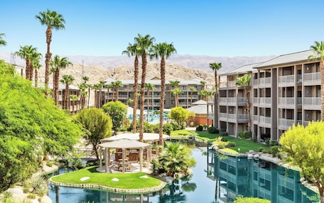 A resort with multiple-story buildings, a swimming pool, and palm trees.
